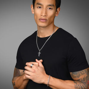 a handsome man in a black shirt shows the silvercross necklace he's wearing
