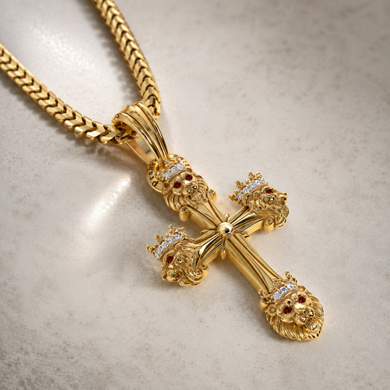 A gold cross pendant necklace with lion heads and small red and clear gemstone details, resting on a light beige stone surface.