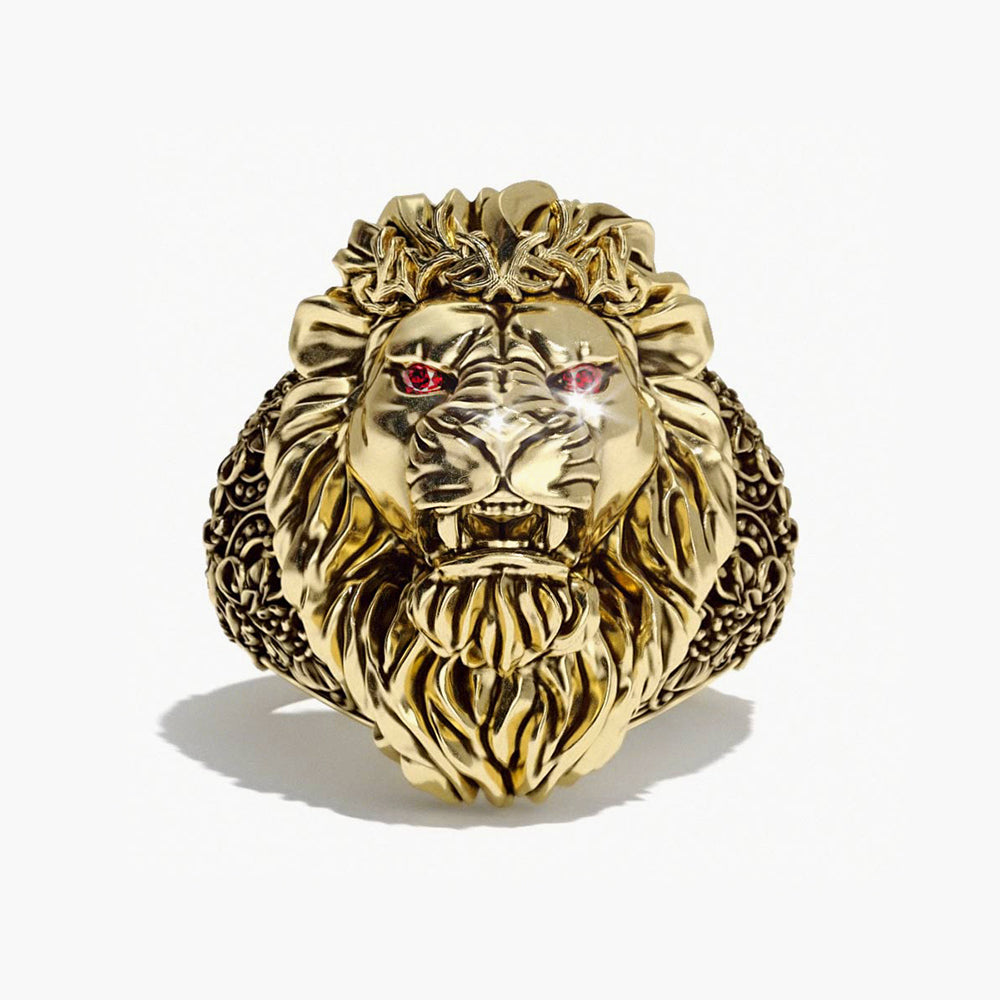 A gold lion ring with ruby eyes sits on a white surface