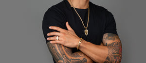 A tattooed man wears mens gold jewelry collections, including a gold franco chain and diamond wedding band