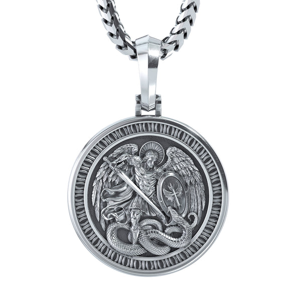 A silver-toned round pendant necklace featuring an embossed relief of Saint Michael with wings and a sword fighting a serpent, suspended from a thick curb chain against a plain white background.
