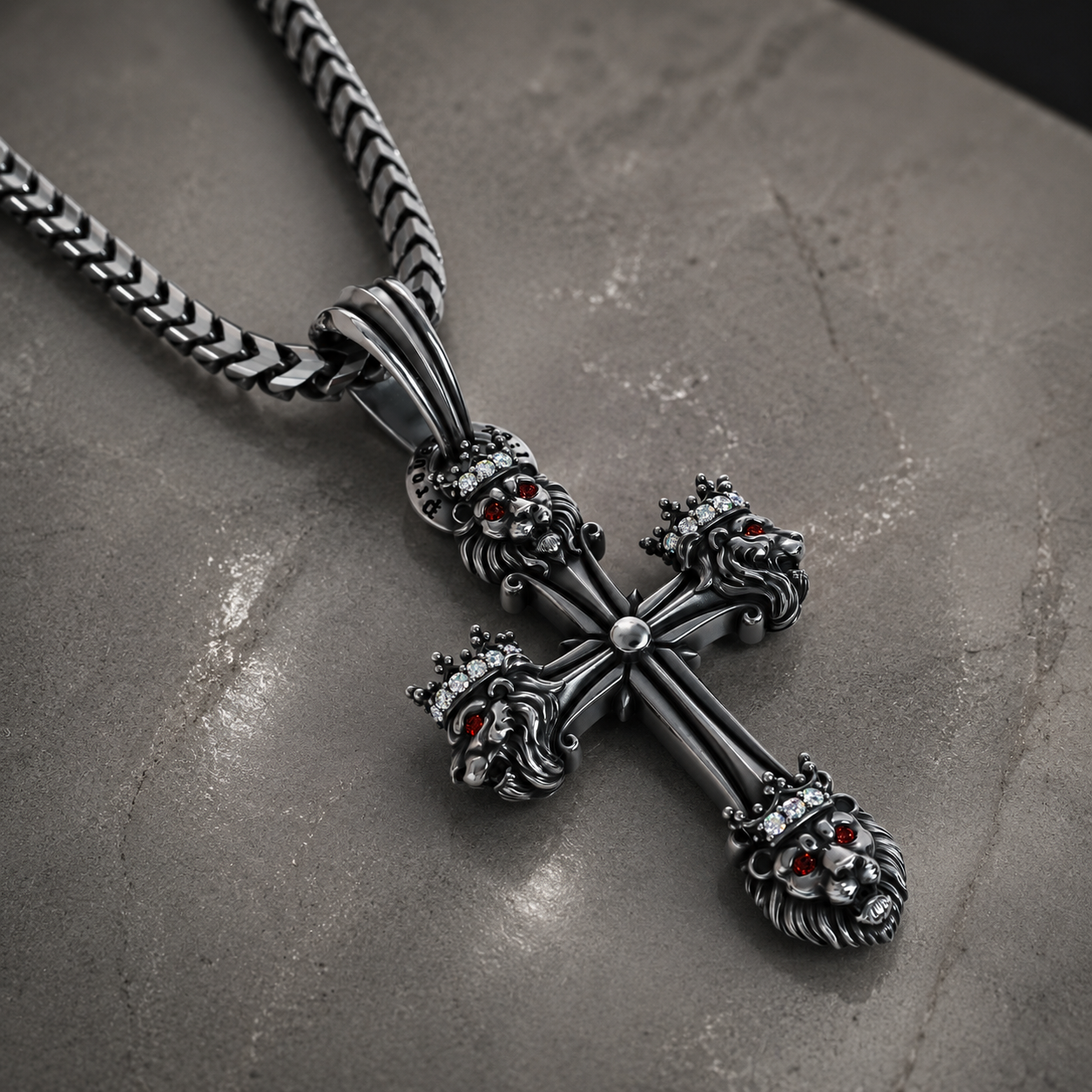 A dark silver cross pendant necklace with lion heads and red gemstone eyes, resting on a textured gray stone surface.