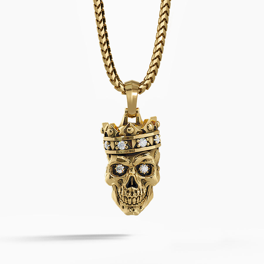 a mens gold pendant in the shape of a skull wearing a crown hangs from a necklace