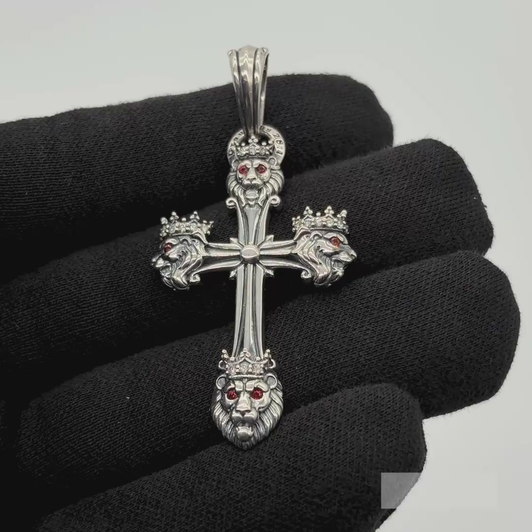 A silver gothic cross pendant with lion heads, diamonds, and garnets is shown