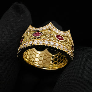a gold crown ring with fleur-de-lis designs, diamonds, and rubies, is held in a hand