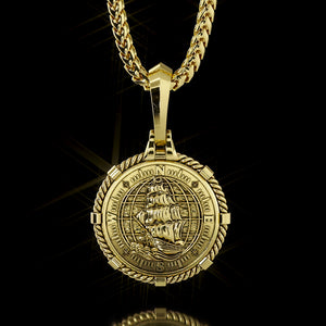 The back of a gold compass pendant features a nautical ship, waves and globe