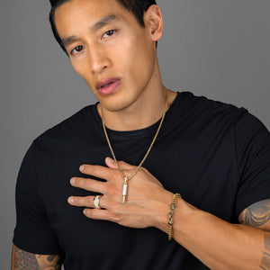 a tattooed man holds up a gold bullet necklace. The bullet is covered with diamonds