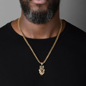 a large gold wolf pendant with diamond eyes hangs from a mans necklace