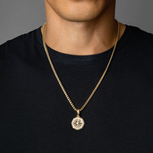 a man in a black shirt wears a gold compass necklace with diamonds