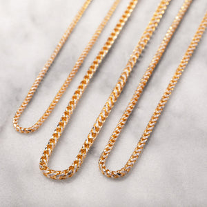 three gold prism cut franco chains lying on white marble