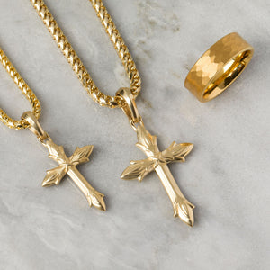 two gold necklaces crosses shine as they lie on a white marble surface