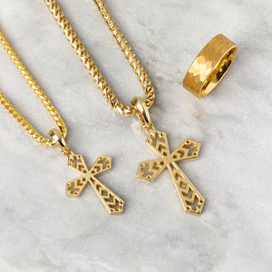 two gold necklaces crosses shine as they lie on a white marble surface next to a gold tungsten ring