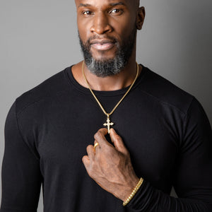 a 14k gold cross pendant is worn by a muscular man with a black shirt as he holds it in his hand