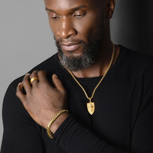 a man touching his shoulder wears a shining shield shaped gold lion pendant and matching gold bracelet