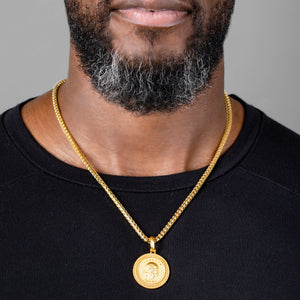 a man in a black shirt wearing a gold necklace and large gold skull pendant