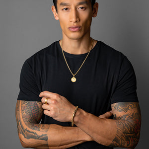 man in a black shirt wearing a gold necklace, gold skull ring and pendant