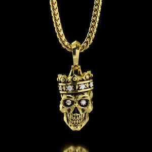 a mens gold pendant in the shape of a skull wearing a crown hangs from a necklace