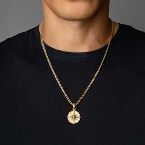 a man in a black shirt wears a gold compass necklace