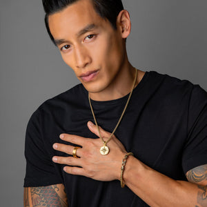 an active man with tattoos wears a gold compass necklace on a thin mens gold chain