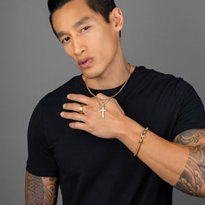 a fit guy in a black shirt holds the gold cross pendant he's wearing with a matching gold bracelet