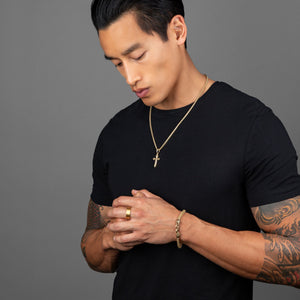 active man prays on the gold cross pendant he's wearing with a matching gold bracelet