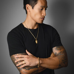 an active man in a black shirt wears a gold crown ring and lion necklace
