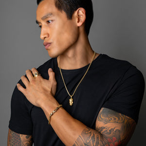 a fit man with tattoos wearing a gold skull pendant, skull ring and gold chain