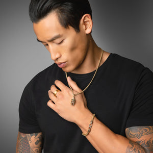 a tattooed man holding up a gold Spartan necklace