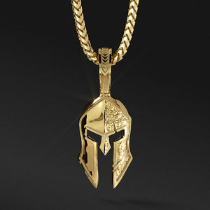 a gold Spartan pendant in the shape of a helmet with one side battle worn