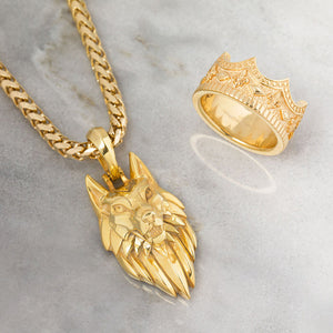 a gold crown ring sits on white marble next to a wolf pendant