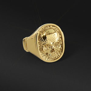 a gold skull ring lies on a black surface