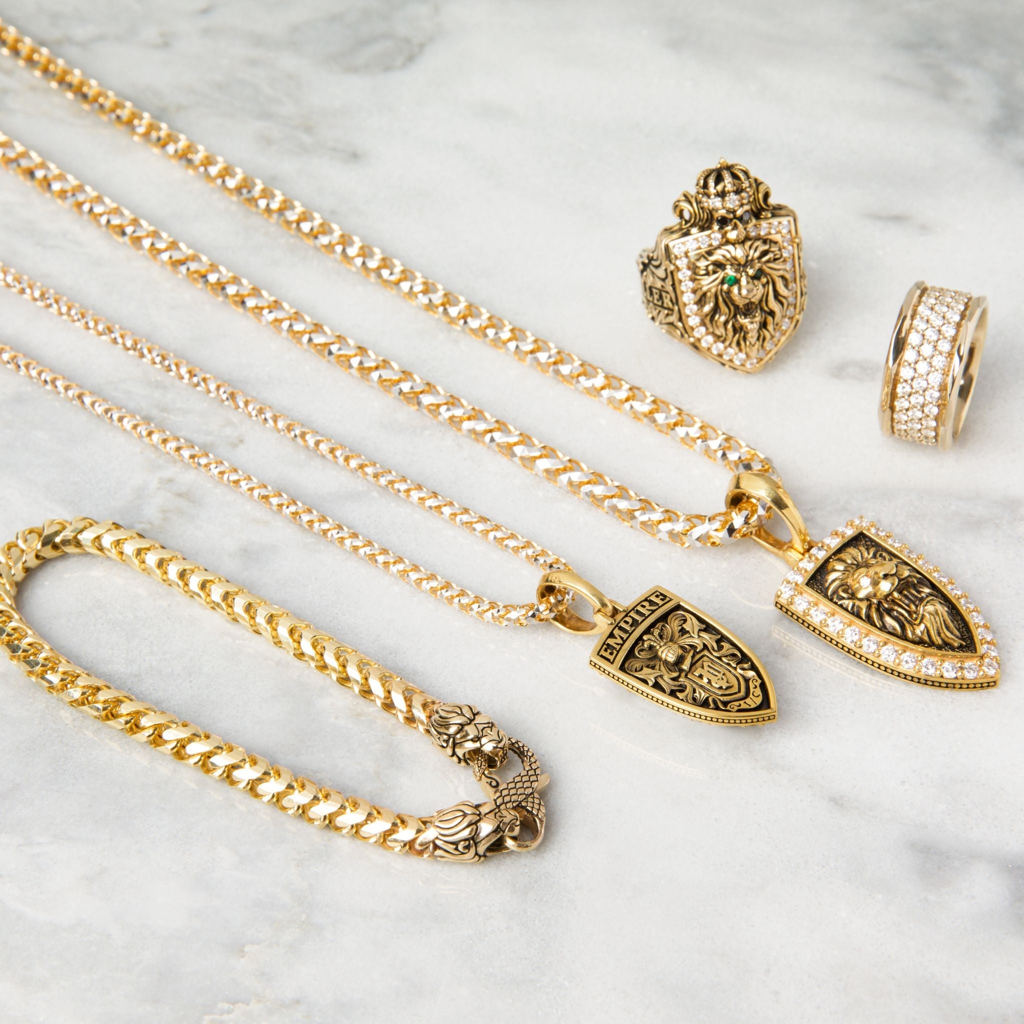 a collection of mens gold jewelry, including an 6.5mm diamond cut franco bracelet lays on white marble