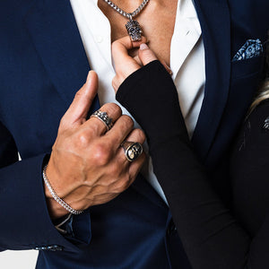 a woman admires the man's silver skull pendant while he grips his suit and a silver bracelet shines