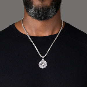 a large sterling silver compass pendant hangs from a mens necklace