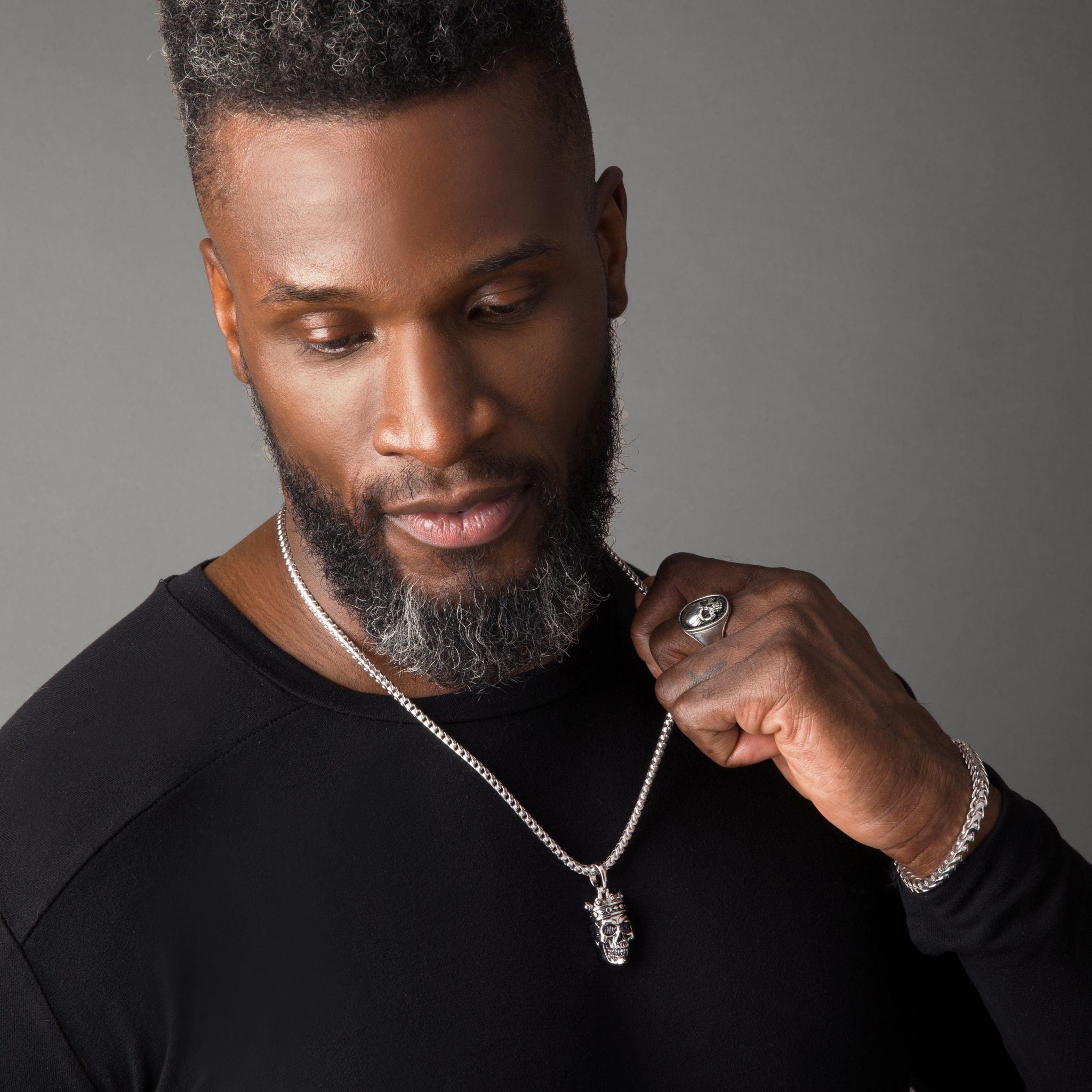 a man wears a polished sterling silver skull pendant and matching skull signet ring