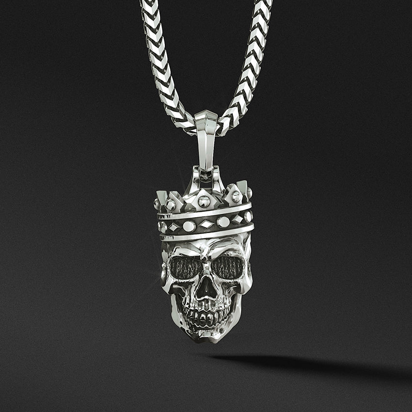 a cool silver mens pendant in the shape of a skull wearing a crown hangs from a necklace