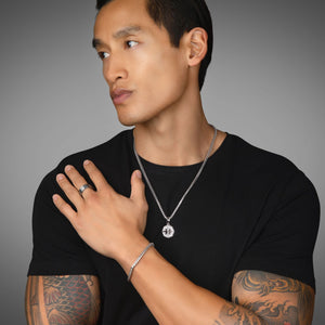 an active man with tattoos wears a silver compass necklace on a silver chain