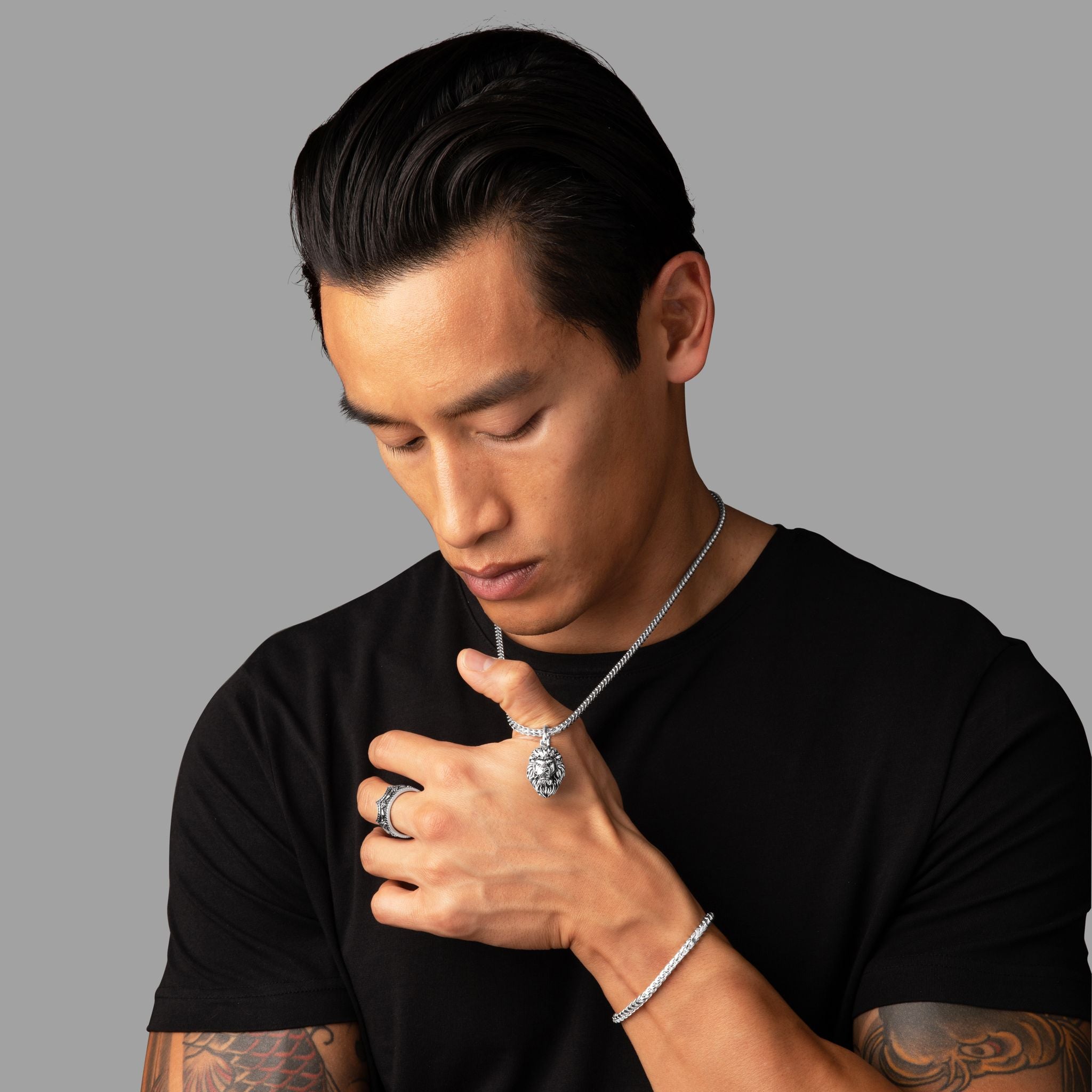 a man in a black shirt pulls on a silver lion pendant hanging from a silver chain around his neck