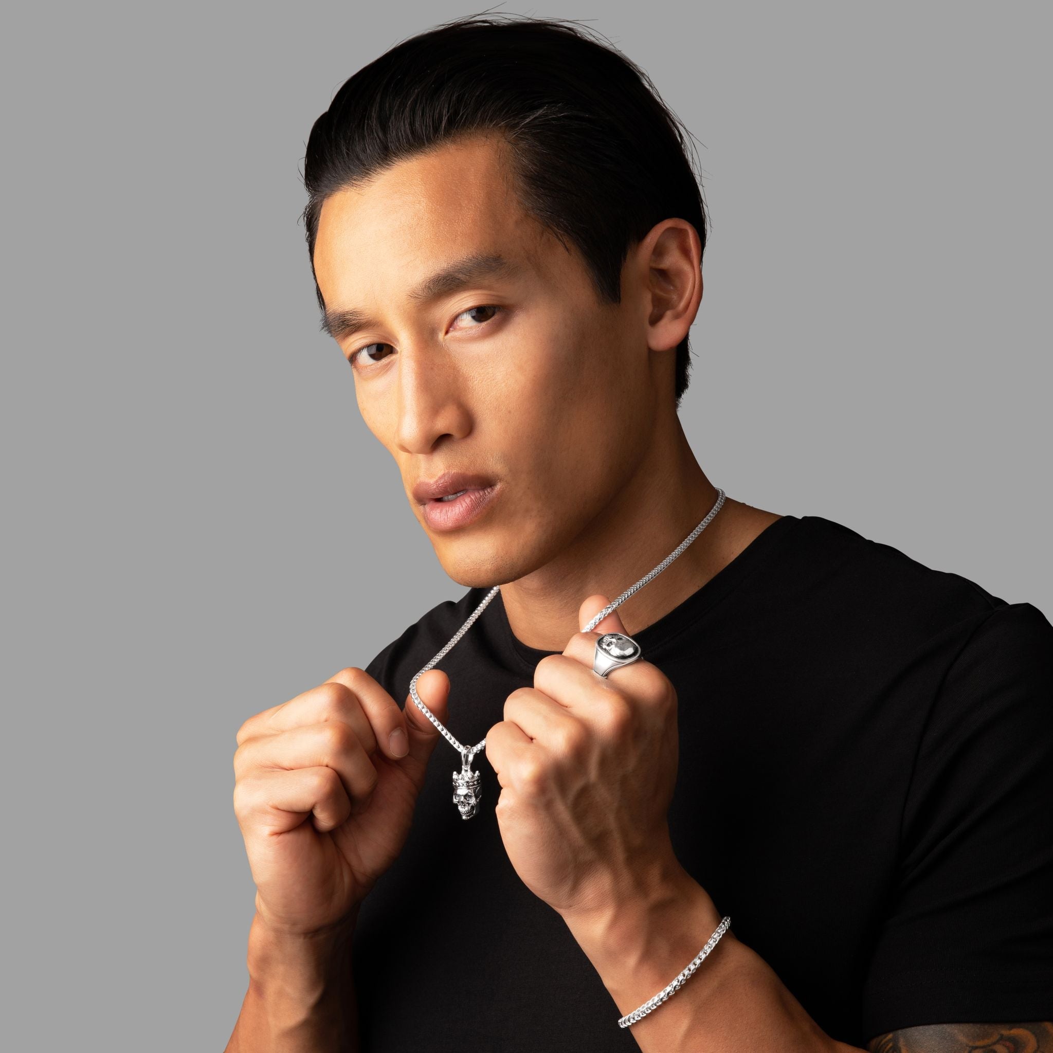 man in a black shirt wearing a silver necklace, skull ring and skull pendant