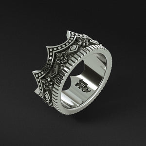 a silver crown ring with antiquing stands on a dark surface