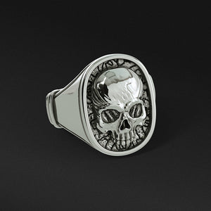 a mens signet ring with a half jaw silver skull lays on a black surface