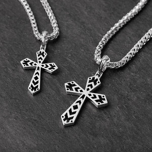 two geometric silver cross chains lie on a slate surface