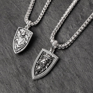 two silver lion pendants lying on slate. One of them shows the heraldic patterns and swords on the back