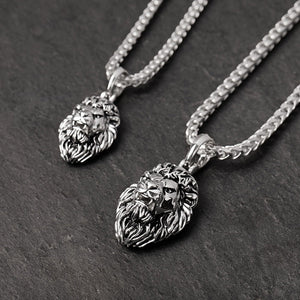 two sterling silver lion pendants lie on a black slate surface