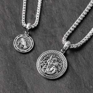 Two silver pendants, one showing Saint Christopher and the other with praying hands reading protect us