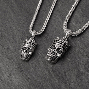one small and one large sterling silver skull pendant lay on a dark slate surface